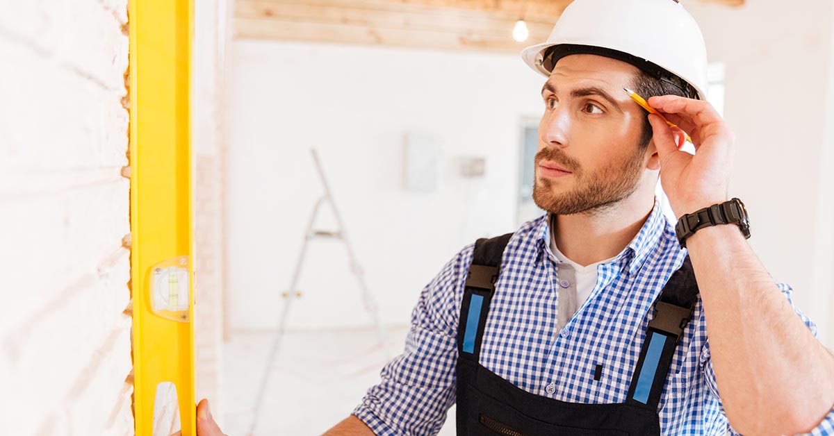 Ein Bauarbeiter mit Schutzhelm, Wasserwaage und Bleistift - Günstig bauen